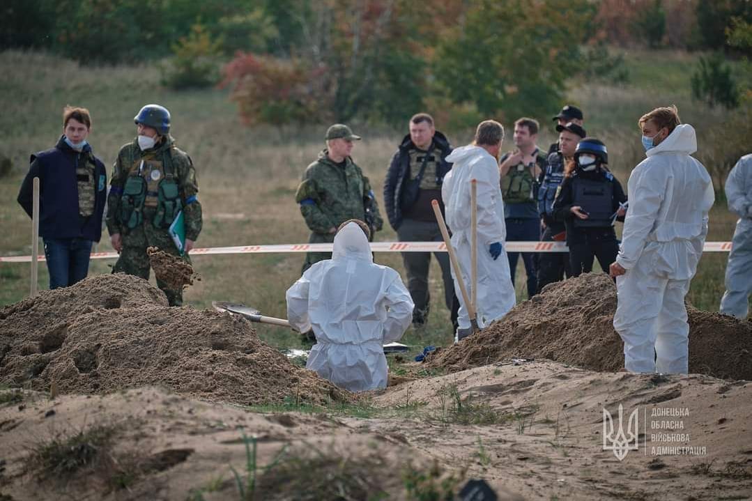 Einsatzkräfte in weißen Schutzanzügen bei den entdeckten Gräbern: Die Exhumierung hat bereits begonnen.