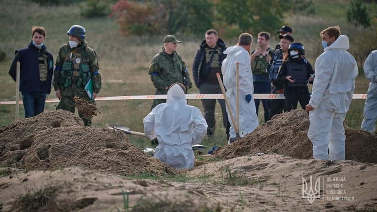 Einsatzkräfte in weißen Schutzanzügen bei den entdeckten Gräbern: Die Exhumierung hat bereits begonnen.