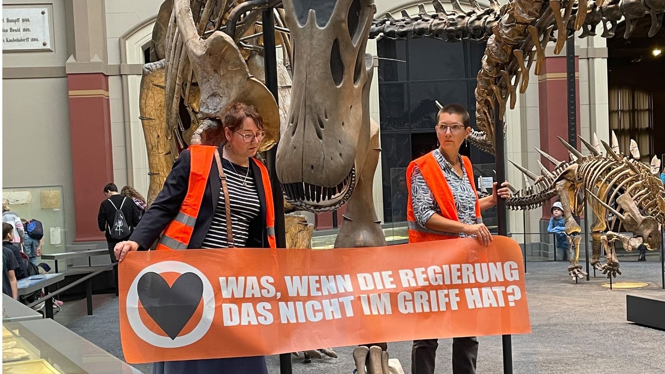Zwei Klimaaktivistinnen im Naturkundemuseum: Auf ihrem Banner steht: "Was, wenn die Regierung das nicht im Griff hat?"