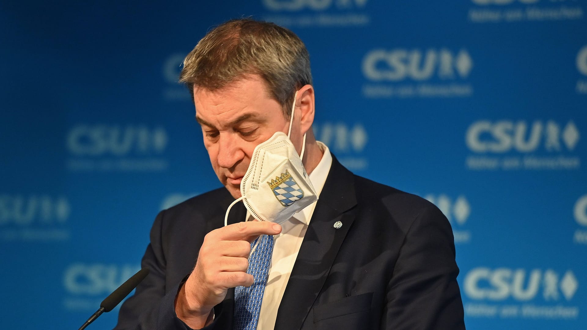 Markus Söder zieht seine FFP2-Maske bei einer Pressekonferenz aus (Archivbild): Nun denkt der Ministerpräsident laut über ein Ende der Maskenpflicht im Nahverkehr nach.