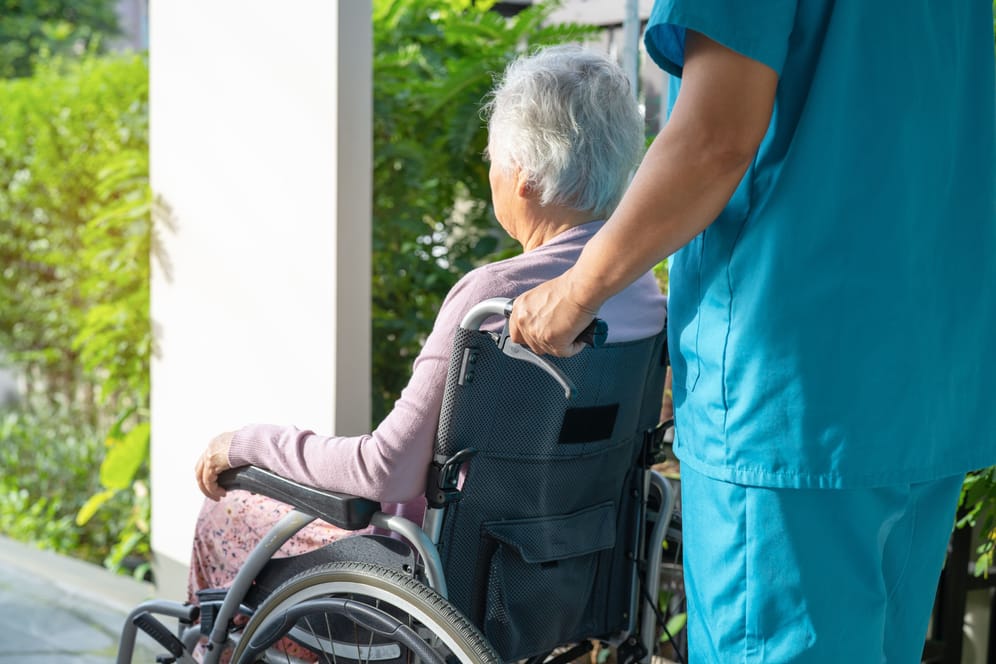 Eine Mitarbeiterin hilft einer Pflegebedürftigen mit ihrem Rollstuhl (Symbolbild): Eine Mitarbeiterin eines Heims in Hildesheim soll Bewohner getötet haben.