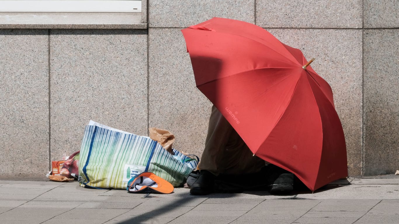 Ein Wohnungsloser sitzt mit einem Regenschirm an der Straße (Symbolbild): Am Nürnberger Hauptbahnhof ist ein Obdachloser am Wochenende attackiert worden.