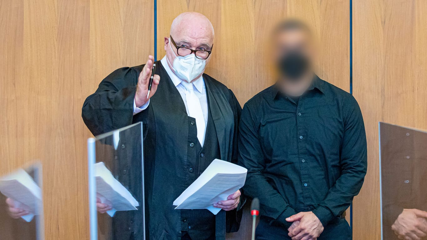 Der Angeklagte (r) steht bei Prozessauftakt neben seinem Verteidiger Matthias Waldraff in einem Saal vom Landgericht Hildesheim.