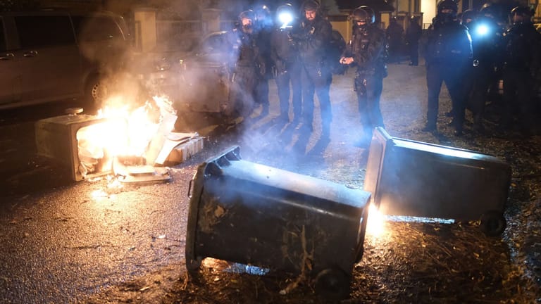 Nach Zusammenstößen in Leipzig: Polizisten stehen neben brennenden Mülltonnen.