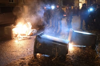 Nach Zusammenstößen in Leipzig: Polizisten stehen neben brennenden Mülltonnen.