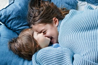 Zwei Kinder kuscheln im Bett miteinander