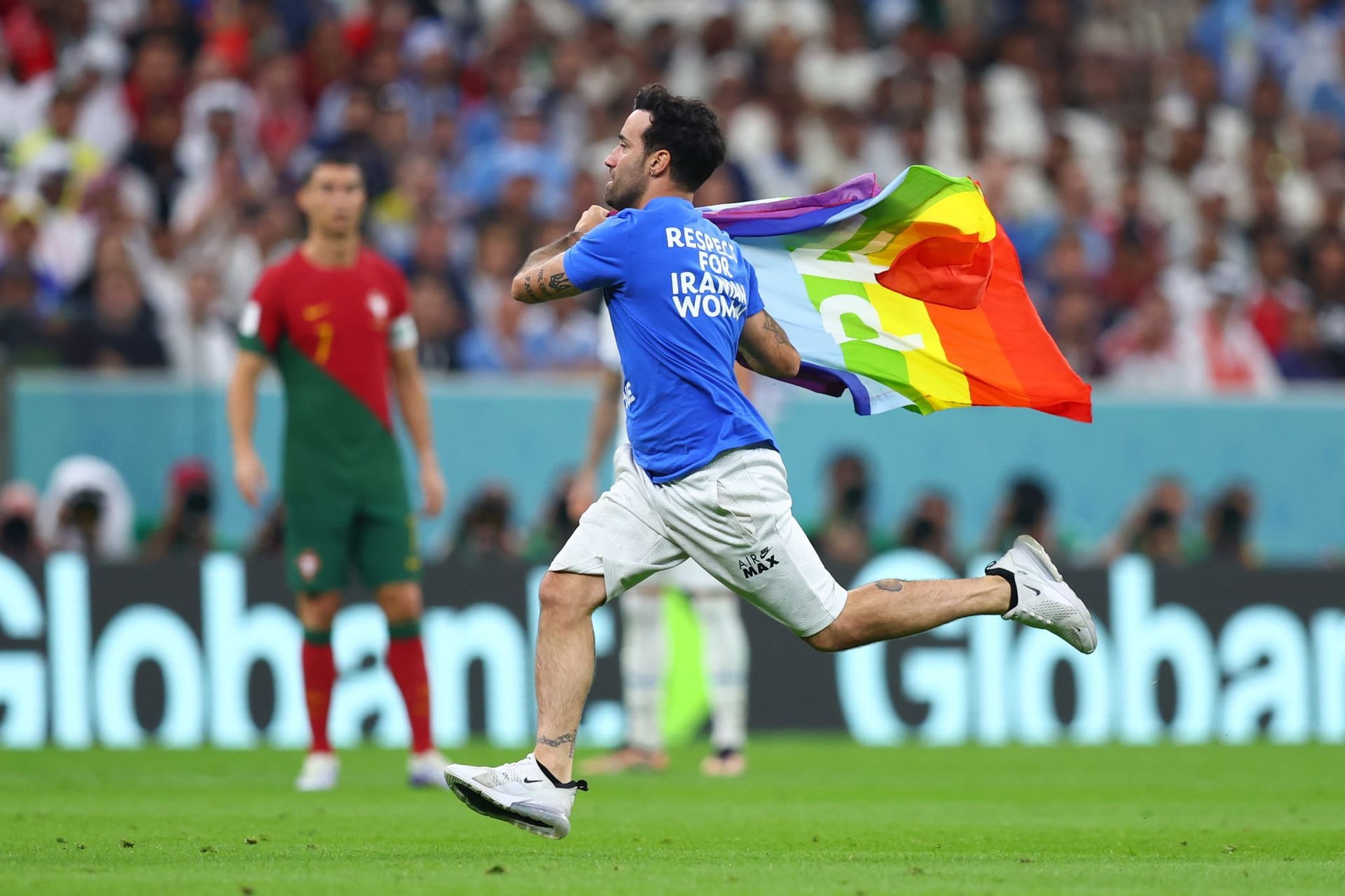 Ein Flitzer mit der Regenbogenflagge und politischen Botschaften zur Ukraine und Iran auf dem T-Shirt läuft über den Rasen.