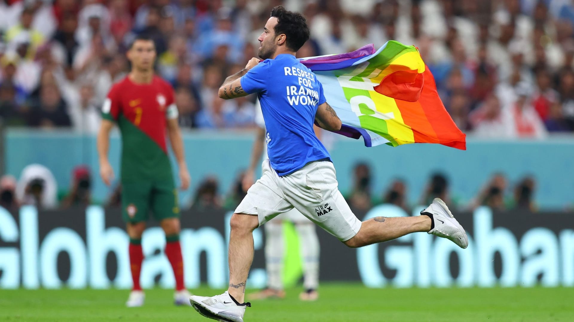 Ein Flitzer mit der Regenbogenflagge und politischen Botschaften zur Ukraine und Iran auf dem T-Shirt läuft über den Rasen.