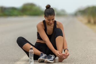 Eine Läuferin sitzt auf dem Boden und hält sich den Fuß.