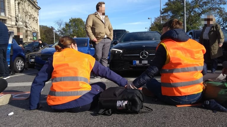 Aktivisten in orangefarbenen Warnwesten sitzen auf der Straße: Der Verkehr um den Stachus liegt lahm.