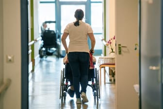 Eine Pflegerin schiebt eine ältere Frau im Rollstuhl (Symbolbild): Seit September 2022 müssen Pflegekräfte nach Tarif bezahlt werden. Die Heime reichen die Kosten weiter.