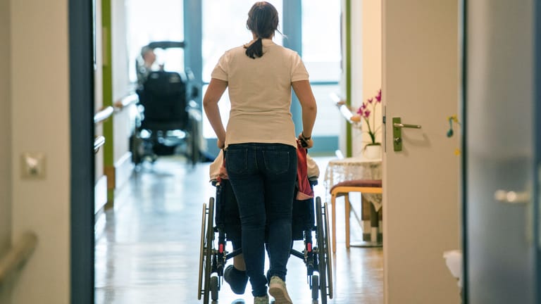 Eine Pflegerin schiebt eine ältere Frau im Rollstuhl (Symbolbild): Seit September 2022 müssen Pflegekräfte nach Tarif bezahlt werden. Die Heime reichen die Kosten weiter.