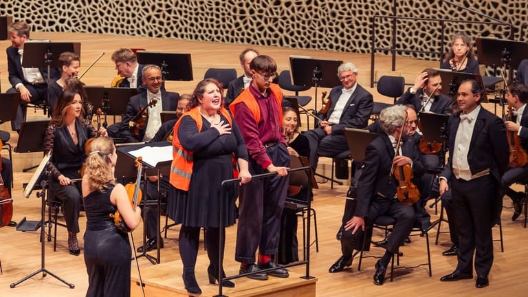 Zwei Aktivisten stehen auf der Bühne der Elbphilharmonie in Hamburg: Sie hatten sich am Dirigentenpult festgeklebt.