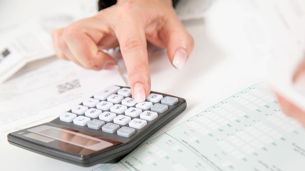 Eine Frau bedient einen Taschenrechner (Symbolbild): Steuern und Sozialabgaben reduzieren das Bruttogehalt.