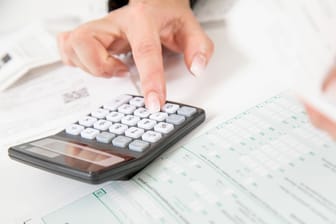 Eine Frau bedient einen Taschenrechner (Symbolbild): Steuern und Sozialabgaben reduzieren das Bruttogehalt.