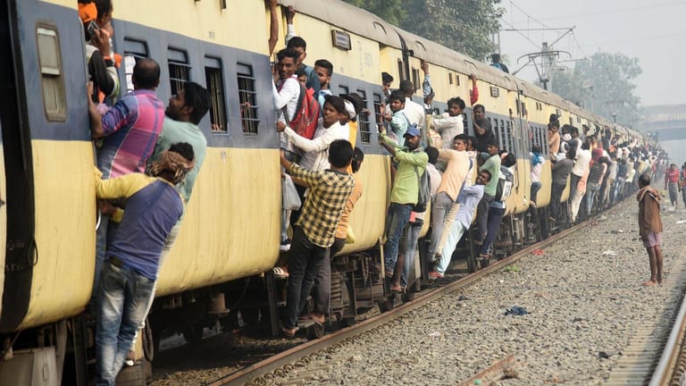 Menschen hängen an den Türen eines stark überfüllten Zuges in Indien: Tickets fürs Bahnfahren ist in Indien spottbillig – und kann gefährlich werden.