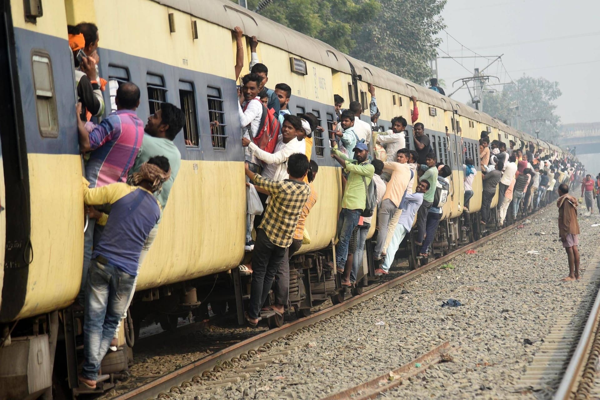 Menschen hängen an den Türen eines stark überfüllten Zuges in Indien: Tickets fürs Bahnfahren ist in Indien spottbillig – und kann gefährlich werden.