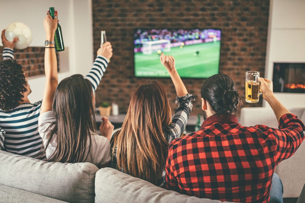 Fußballfans gucken gemeinsam Spiel: Im Winter verlagert sich Public Viewing in die heimischen Wohnzimmer.