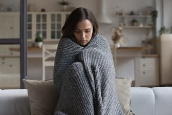 Ein Mädchen sitzt eingehüllt in eine Wolldecke auf dem Sofa.