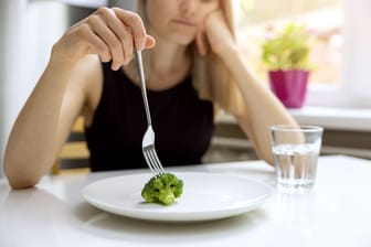 Eine Frau steckt lustlos eine Gabel in ein Stück Brokkoli.