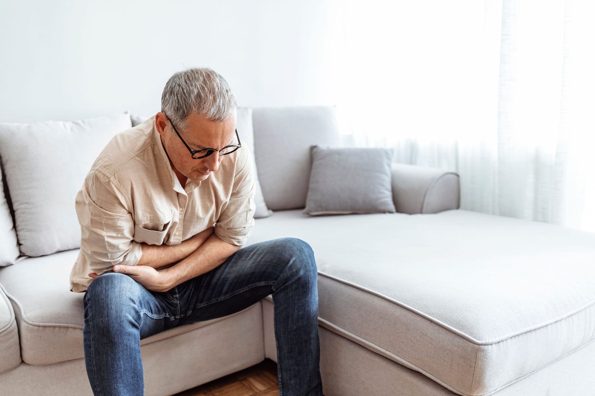 Mann mittleren Alters sitzt mit Bauchschmerzen auf einem Sofa