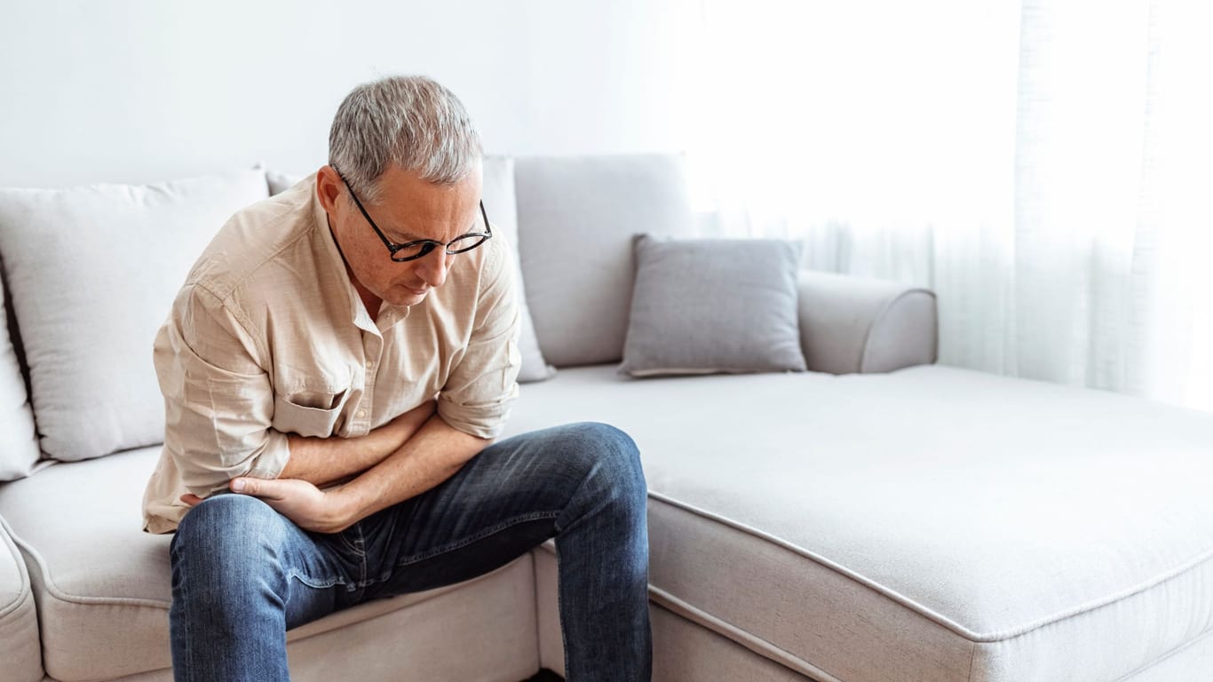 Mann mittleren Alters sitzt mit Bauchschmerzen auf einem Sofa