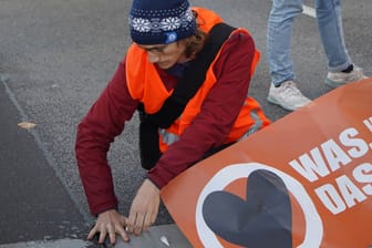 Ein festgeklebter Klimaaktivist auf einer Berliner Straße (Archivbild): Einem Bericht zufolge führt die Polizei viele von ihnen als Mehrfachtäter.