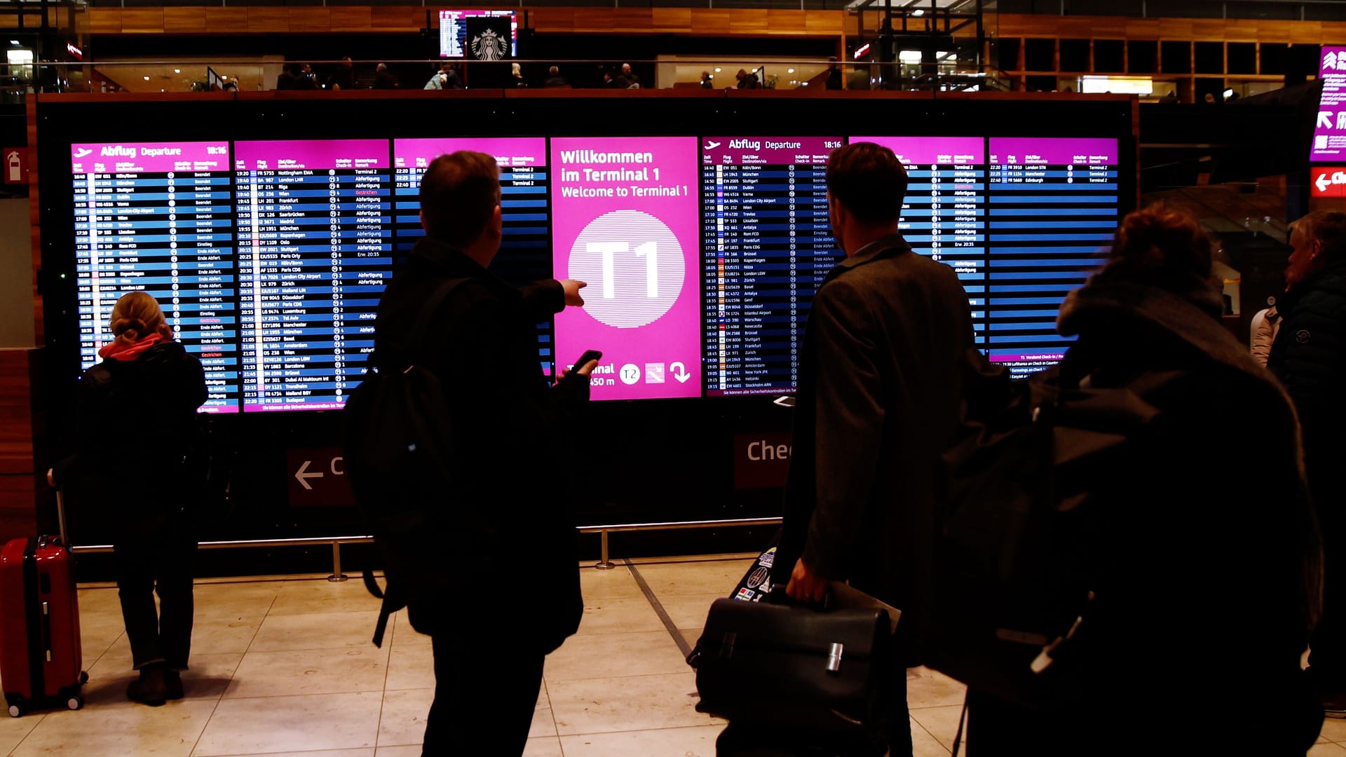 Fluggäste stehen am Flughafen BER vor Anzeigetafeln.