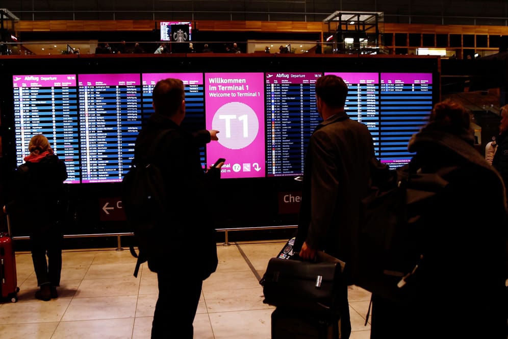 Fluggäste stehen am Flughafen BER vor Anzeigetafeln.
