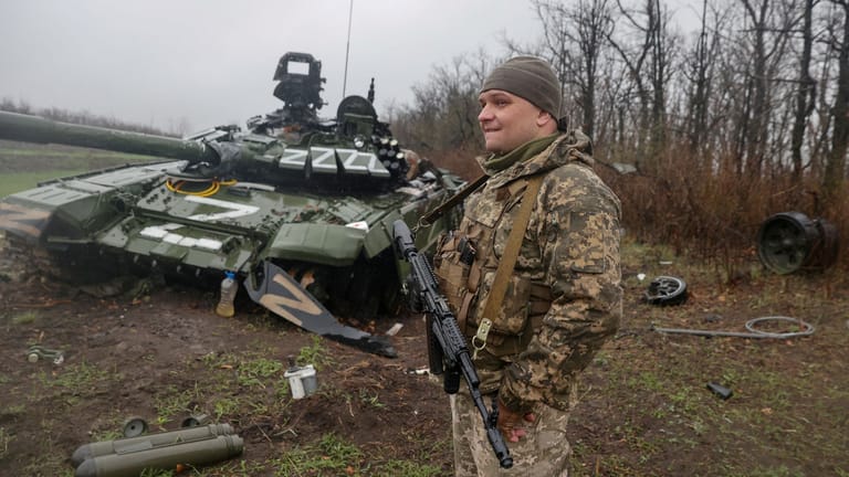 Ein ukrainischer Soldat steht neben einem zerstörten russischen Panzer.
