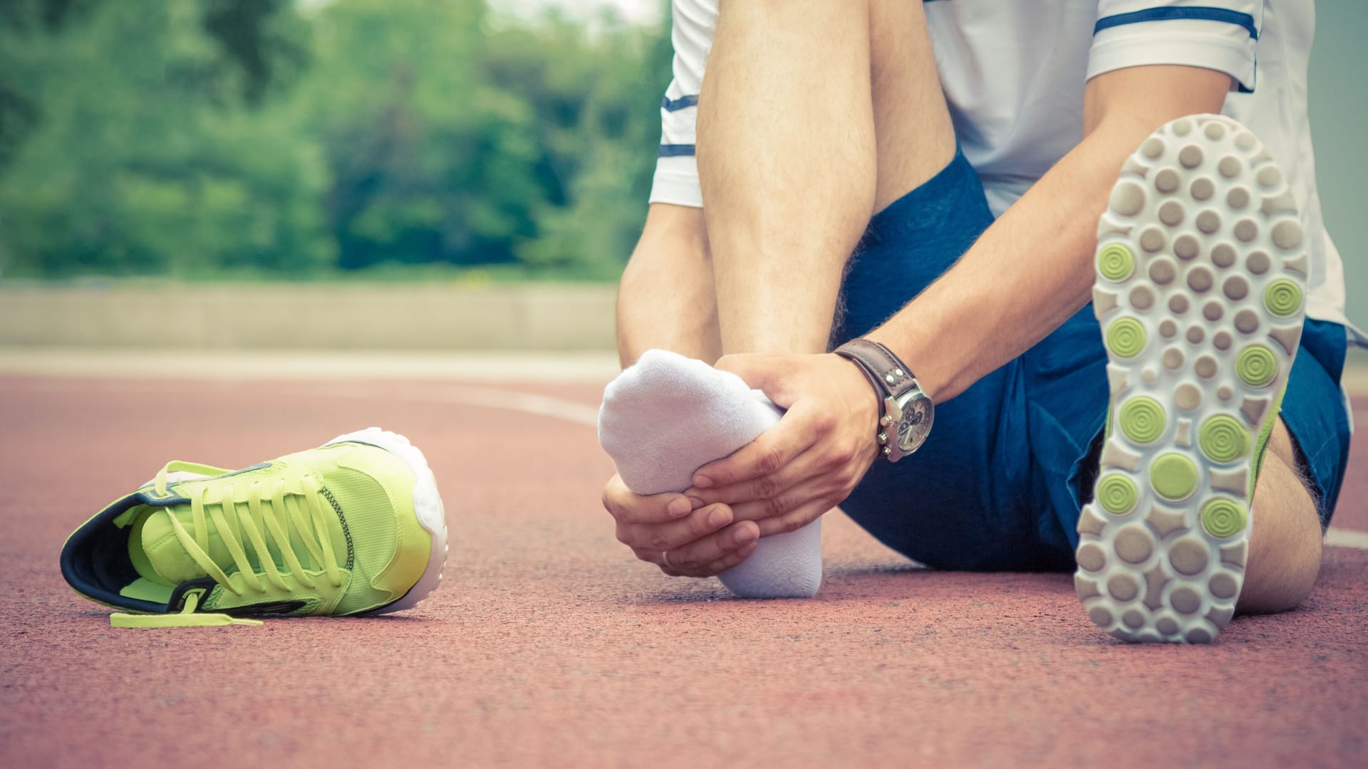 Ein Jogger sitzt auf dem Boden und hält sich den Fuß.