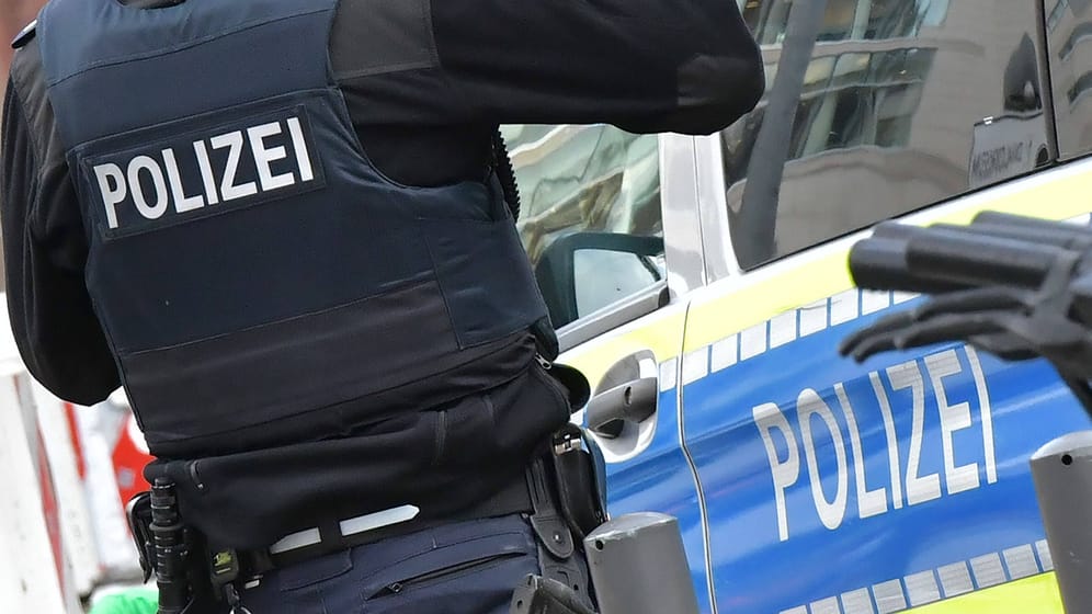 Ein Polizist vor einem Streifenwagen (Symbolbild): Nach einer Raubserie wurde ein 14-Jähriger festgenommen.