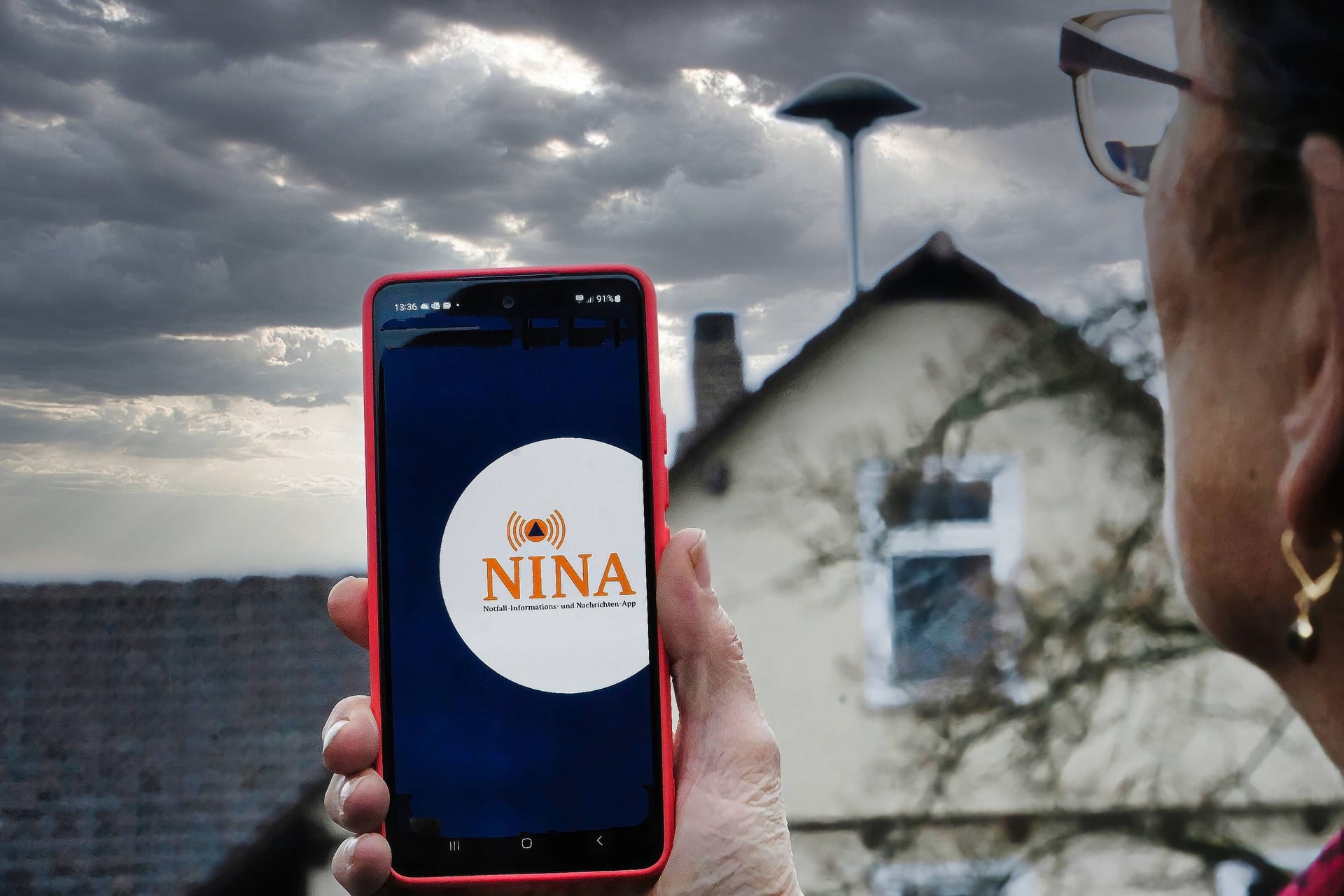 Eine Frau blickt auf eine Sirene und hat die Warn-App Nina auf ihrem Handy geöffnet (Symbolbild): Am Donnerstag geht der Warntag in die zweite Runde.