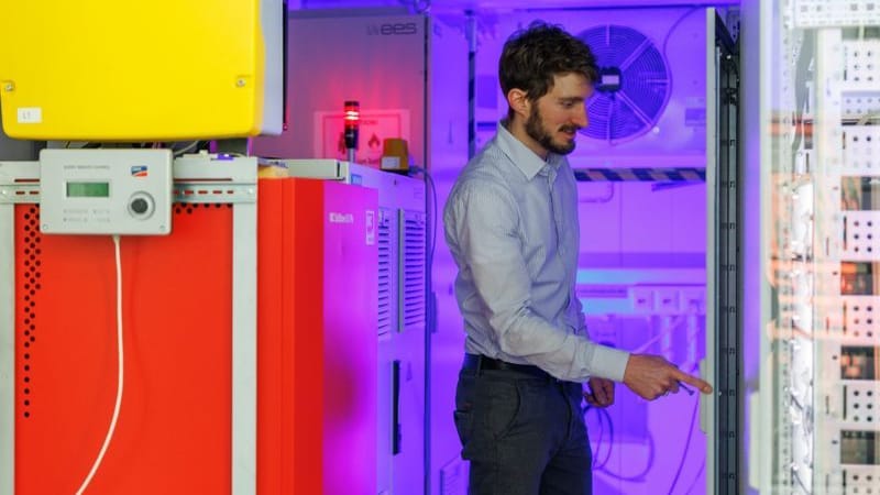 Simon Resch, wissenschaftlicher Mitarbeiter am Lehrstuhl für Elektrische Energiesysteme (LEES) der FAU, vor einem Batteriespeichersystem. Simon Resch, wissenschaftlicher Mitarbeiter am Lehrstuhl für Elektrische Energiesysteme (LEES) der FAU, vor einem Batteriespeichersystem.