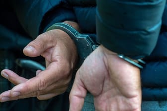 Ein Mann trägt Handschellen (Symbolfoto): Neben einer Machete machten die Beamten noch weitere Entdeckungen in der Wohnung des Angreifers.