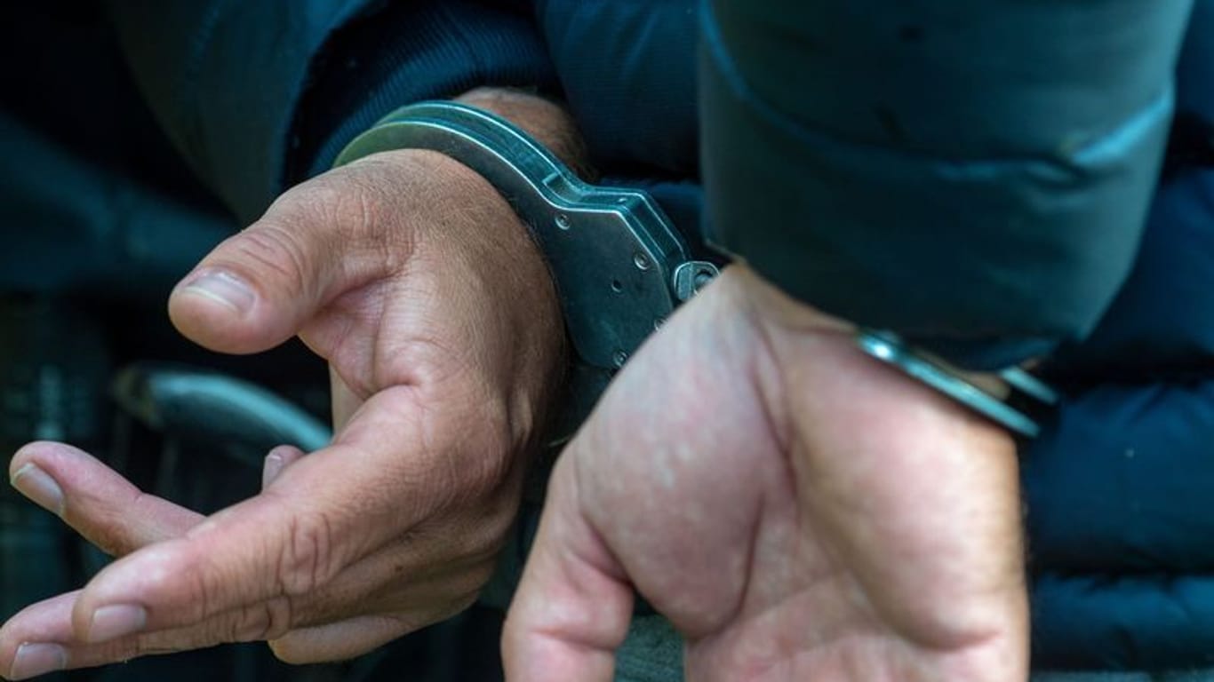 Ein Mann trägt Handschellen (Symbolfoto): Neben einer Machete machten die Beamten noch weitere Entdeckungen in der Wohnung des Angreifers.