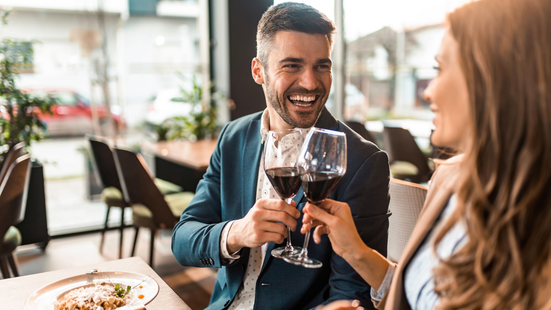 Eine Frau und ein Mann stoßen beim Essen mit einem Glas Rotwein an.