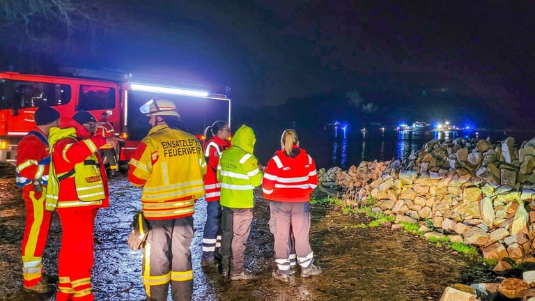 Feuerwehrleute stehen am Ufer des Rheins: Ein Schiff stand in Flammen.