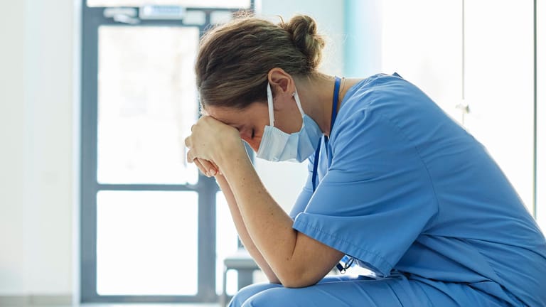 Eine erschöpfte Pflegerin sitzt auf einem Flur (Symbolbild): Das deutsche Gesundheitssystem ist stark belastet.
