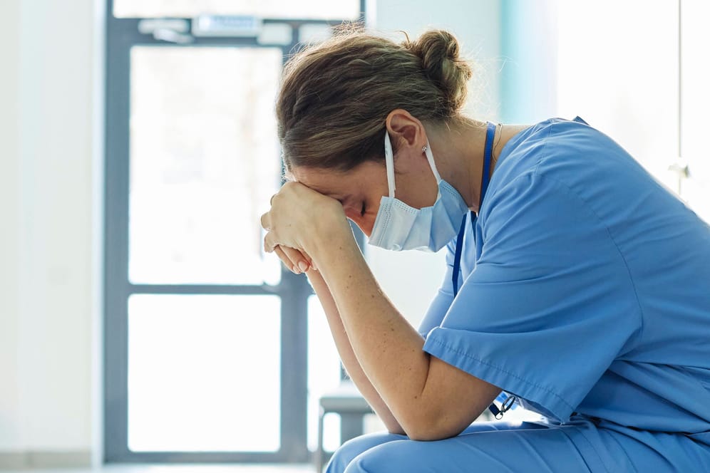 Eine erschöpfte Pflegerin sitzt auf einem Flur (Symbolbild): Das deutsche Gesundheitssystem ist stark belastet.