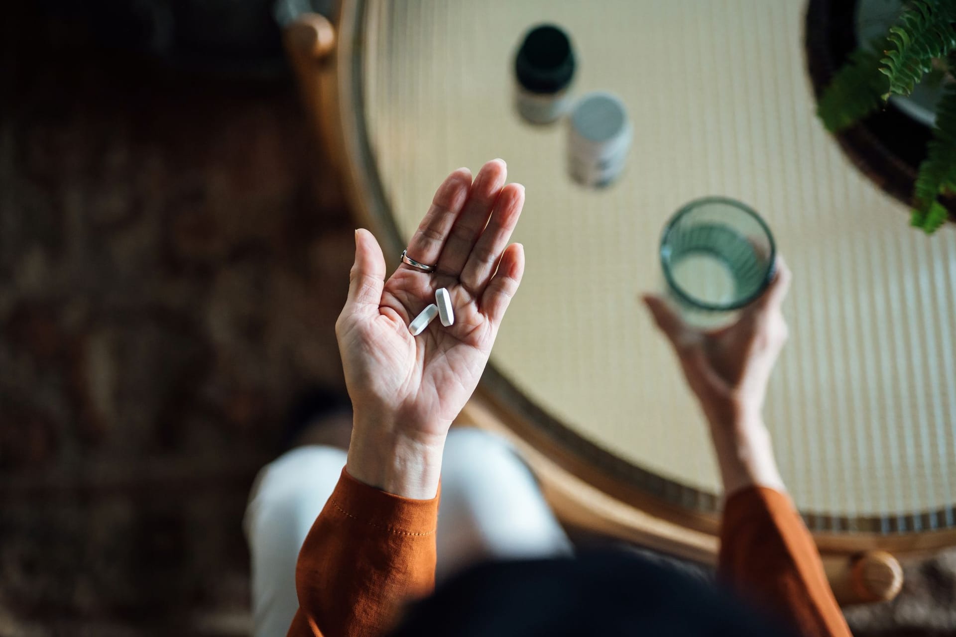 Hände einer älteren Person; in der linken Hand Tabletten, in der rechten ein Glas Wasser