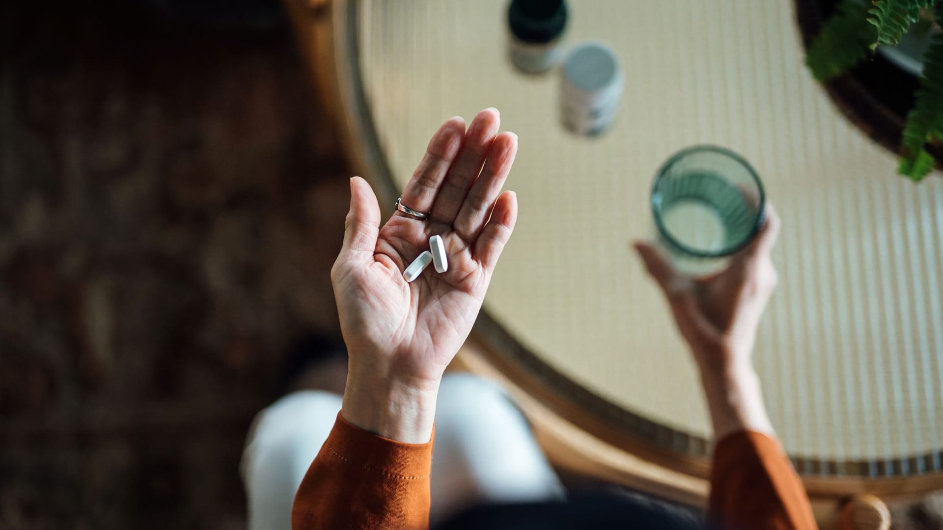 Hände einer älteren Person; in der linken Hand Tabletten, in der rechten ein Glas Wasser