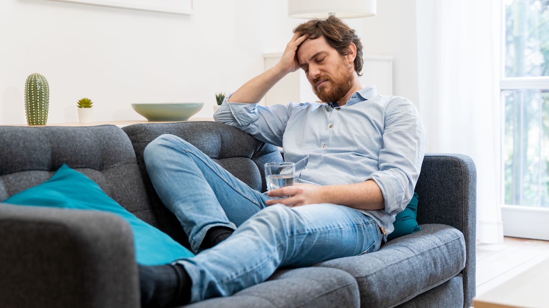 Ein Mann sitzt auf dem Sofa und hält sich die Hand an die Stirn.