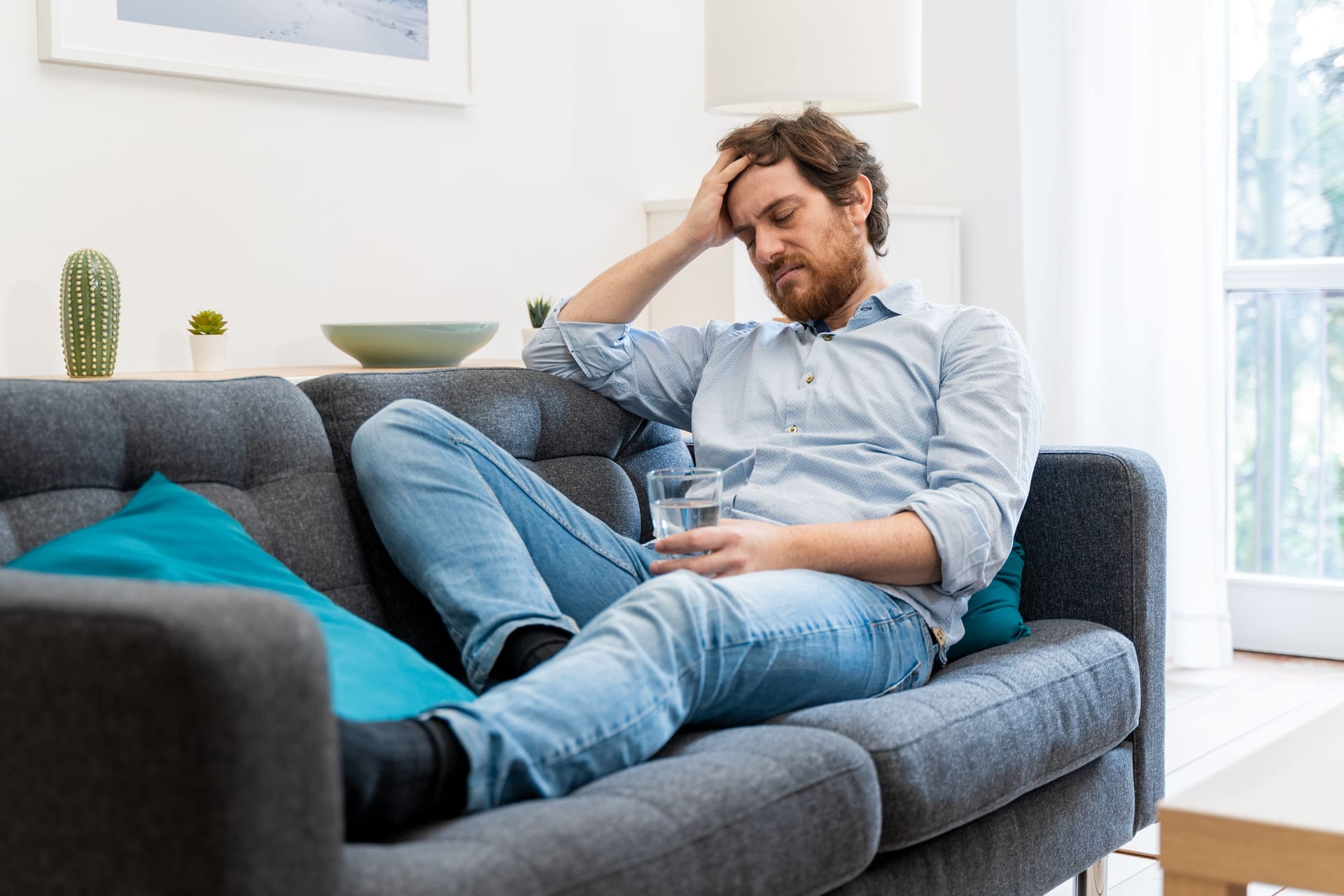 Ein Mann sitzt auf dem Sofa und hält sich die Hand an die Stirn.