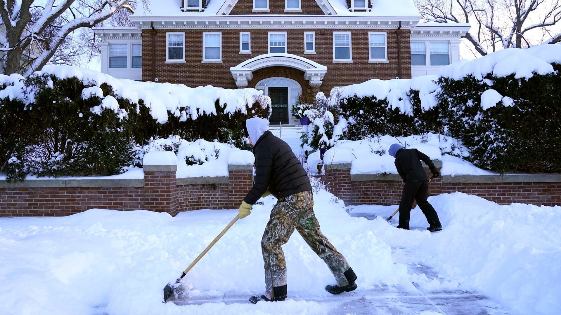 Minneapolis: Kinder schaufeln Schnee von einem Gehweg vor einer Einfahrt.