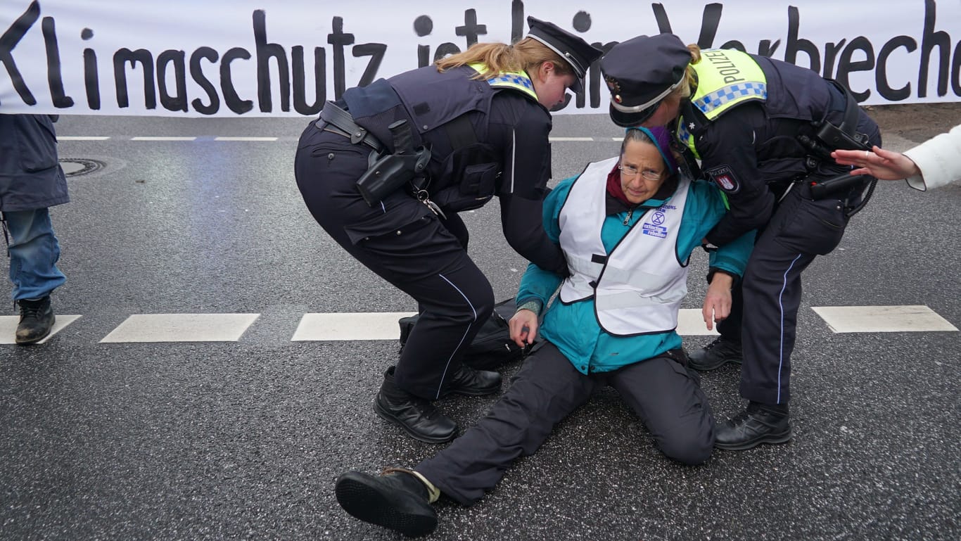 Eine Aktivistin wird von Polizistinnen weggetragen: Zuvor wollte die Frau sich an der Straße festkleben.
