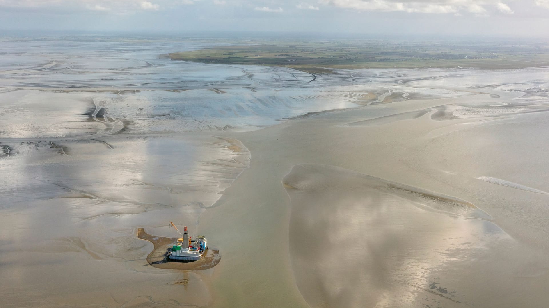 Luftaufnahme der Bohrinsel im Wattenmeer bei Ebbe: Auf dem Festland im Hintergrund liegt die Gemeinde Friedrichskoog im Kreis Dithmarschen.