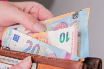 Eine Frau zieht Euroscheine aus einem Portemonnaie (Symbolbild): Die Preisbremsen für Strom und Gas belohnen eifrige Energiesparer zusätzlich.