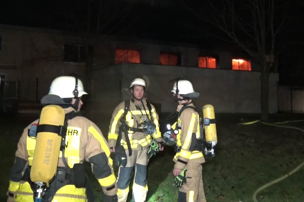 Einsatzkräfte vor der Turnhalle: In den Fenstern sind die Flammen zu sehen.