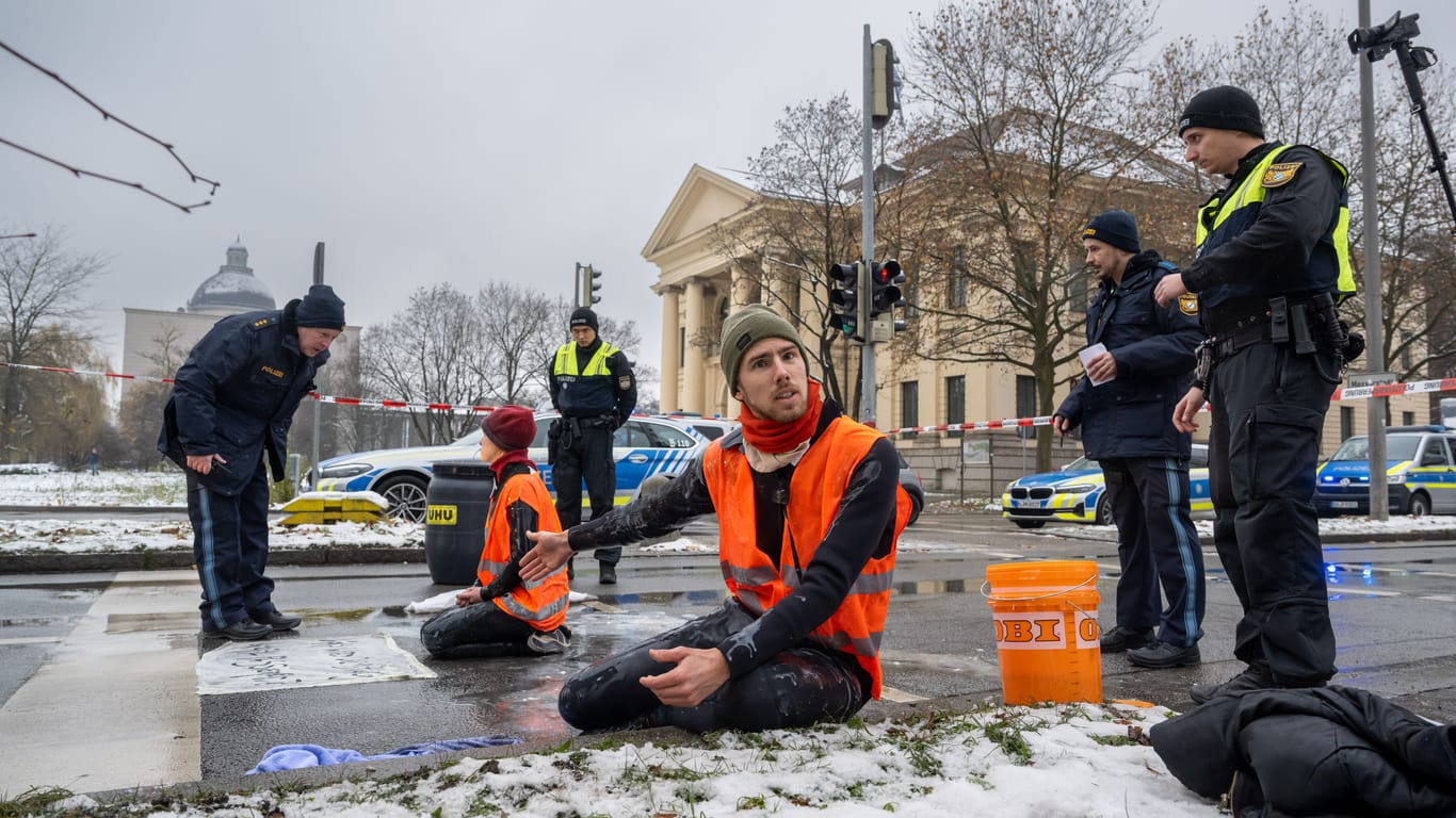 Zwei Klimaaktivisten nehmen an einer Protestaktion der Gruppe "Letzte Generation" teil, indem sie versuchen sich auf einer Straße festzukleben. Die Aktion fand trotz einer Allgemeinverfügung der Stadt München zu Klimaprotesten statt.